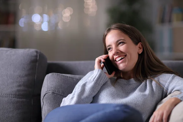 Mulher feliz falando ao telefone em um sofá durante a noite — Fotografia de Stock