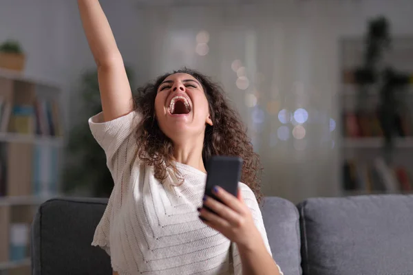Возбужденная женщина празднует успех держа в руках мобильный телефон — стоковое фото