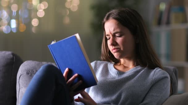 Stressed woman suffering eyestrain reading a book sitting on a couch in the night at — Stock Footage Stressed Woman Suffering Eyestrain Reading Book Sitting Couch Night Video Clip