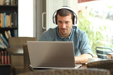 Ciddi bir adam barda kulaklıklı bir laptop kullanıyor.