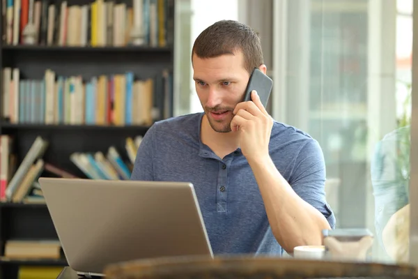 Hombre serio habla por teléfono y utiliza un ordenador portátil —  Fotos de Stock