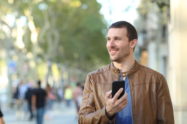 Szczęśliwy człowiek trzyma inteligentny telefon spacery patrząc na bok — Zdjęcie stockowe