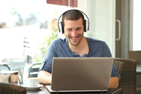 Šťastný muž se sluchátky sledující média na notebooku — Stock fotografie