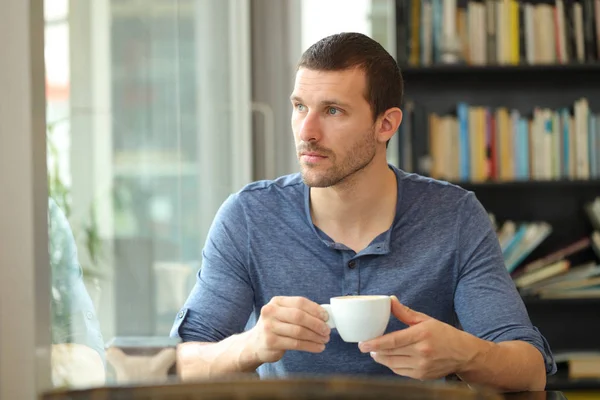 Pensiv man håller kaffe tittar genom ett fönster i en bar — Stockfoto