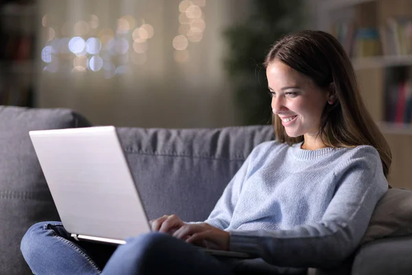 Mulher feliz usando laptop em um sofá em casa à noite — Fotografia de Stock