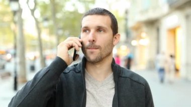 Front view of a serious adult man talking on mobile phone walking towards camera in 
