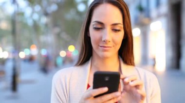 Ciddi bir kadının akşam saatlerinde akıllı telefon içeriğine göz atması ön planda. 