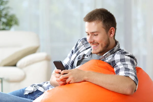 Pria bahagia di rumah menggunakan ponsel di sebuah kantong — Stok Foto