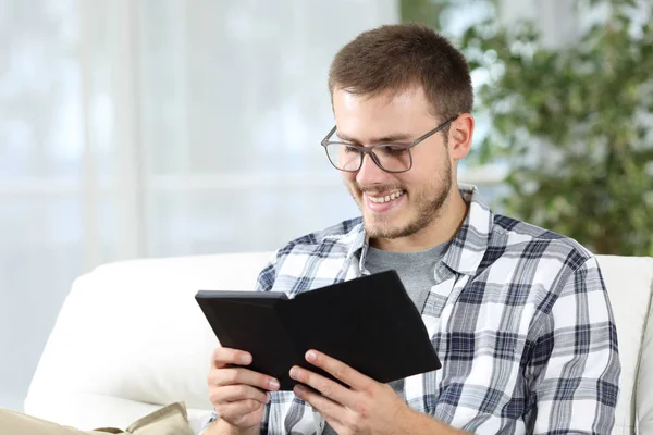 Homem usando óculos lendo um ebook em um sofá — Fotografia de Stock