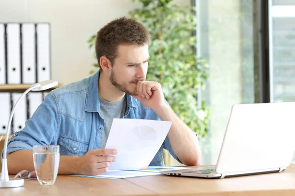 Pensive man holding document reading laptop content — Stock Photo, Image