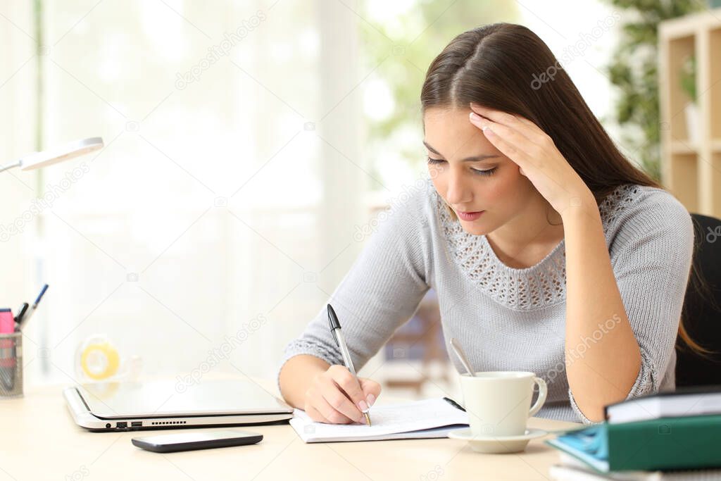 Concentrated woman writing notes on notebook sitting on a desk at home