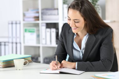 Ofisteki bir masada oturan mutlu yönetici kadın ajandaya notlar yazıyor.