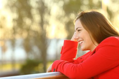 Kırmızı ceketli mutlu kadın gün batımında sahilin yakınındaki bir balkona bakıyor.