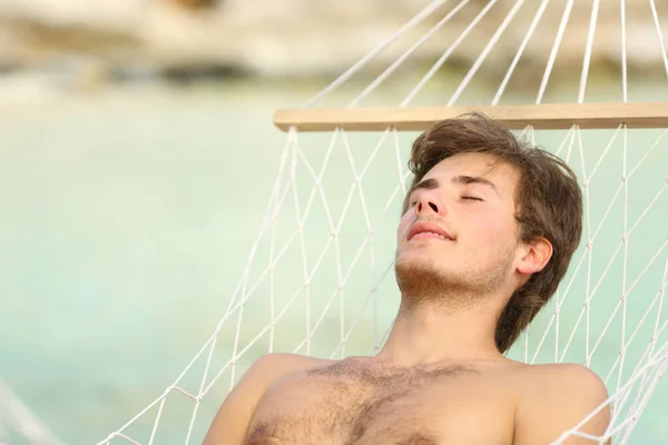 Relaxed shirtless man sunbathing resting on a hammock by the beach
