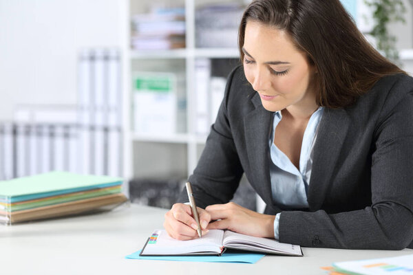 Executive woman writing notes on agenda sitting on a desk at the office