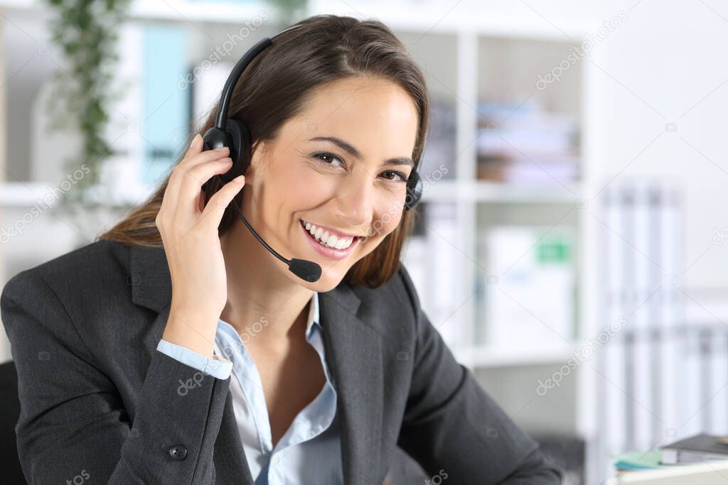 Happy telemarketer woman with headset posing looking at camera sitting on a desk at office