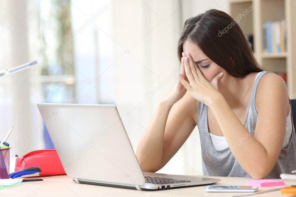 Tired student woman with laptop complaining sitting on a desk in the living room at home