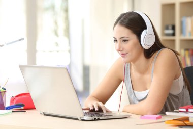 Dizüstü bilgisayarında kulaklık takan ciddi bir öğrenci kadın evde bir masada oturuyor.