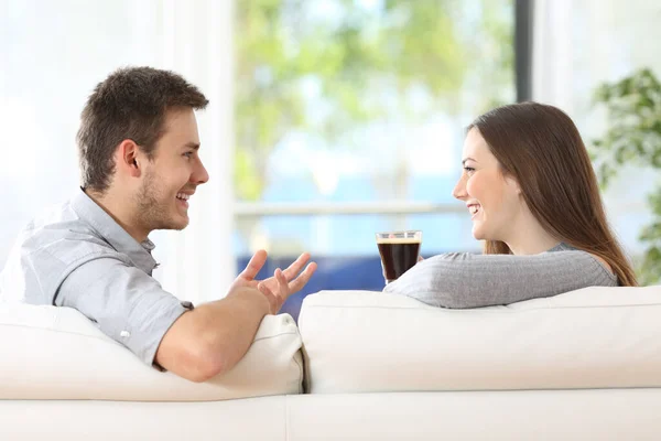 一对快乐的夫妇在家里的沙发边聊天边喝咖啡的照片 — 图库照片