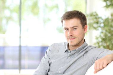 Evdeki kanepede oturmuş kameraya bakan bir gencin portresi.