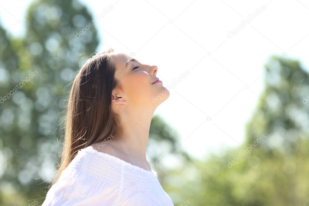 Side view of a relaxed woman breathing fresh air standing outdoors on a green park