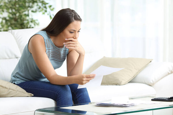 Worried woman reading lettter sitting in the sofa in the living room at home