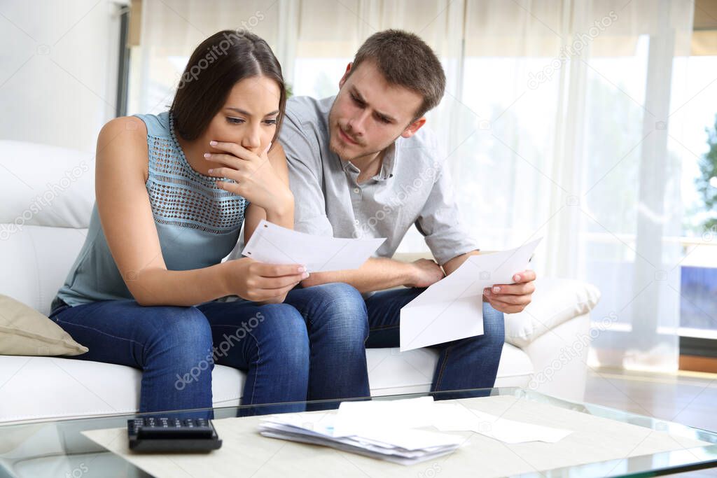 Worried couple checking receipt sitting in the sofa in the living room at home