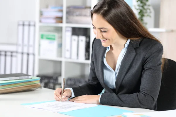 Happy executive woman signs contract sitting on a desk at the office