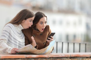 Şaşkın turistler elinde harita olan kadınlar kışın balkonda akıllı telefonları kontrol ediyorlar.