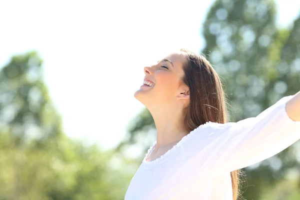 一个快乐的女人在户外呼吸新鲜空气 背靠绿树张开双臂的侧影 — 图库照片