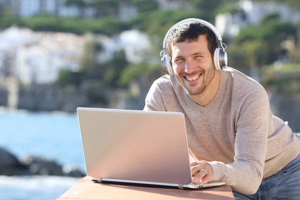 Glad Man Med Hörlurar Och Laptop Poserar Tittar Kameran Stranden — Stockfoto