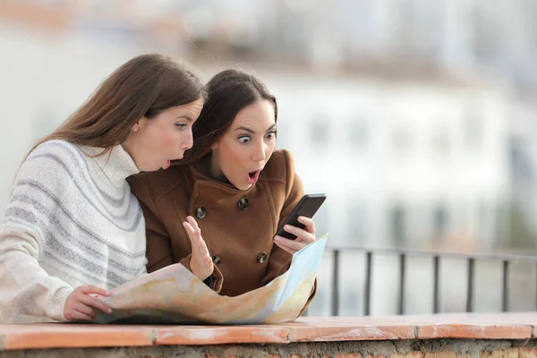 地図を持つ驚きの観光客の女性は冬にバルコニーにスマートフォンをチェック — ストック写真