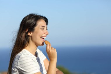 Happy woman eating cookie in a hotel balcony on the beach on summer clipart