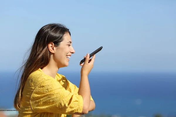 暑假期间 一个快乐女人在海滩上的酒店阳台上用智能手机进行语音识别的照片 — 图库照片