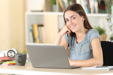 Mutlu öğrenci kameraya bakarak poz veriyor. Evdeki sandalyede oturuyor.