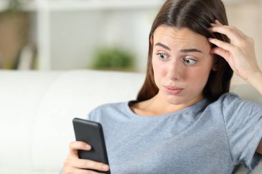 Evde oturma odasındaki koltukta oturan akıllı telefondan hatayı keşfeden şaşkına dönmüş kız.