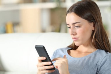 Evdeki oturma odasındaki kanepede oturan akıllı telefonu kullanan bir genç.