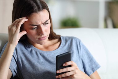 Endişeli kız, evdeki oturma odasındaki koltukta oturan akıllı telefonu kontrol ediyor.