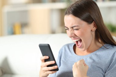 Heyecanlı gençler evdeki oturma odasındaki kanepede oturup cep telefonundan iyi haberleri kontrol ediyorlar.