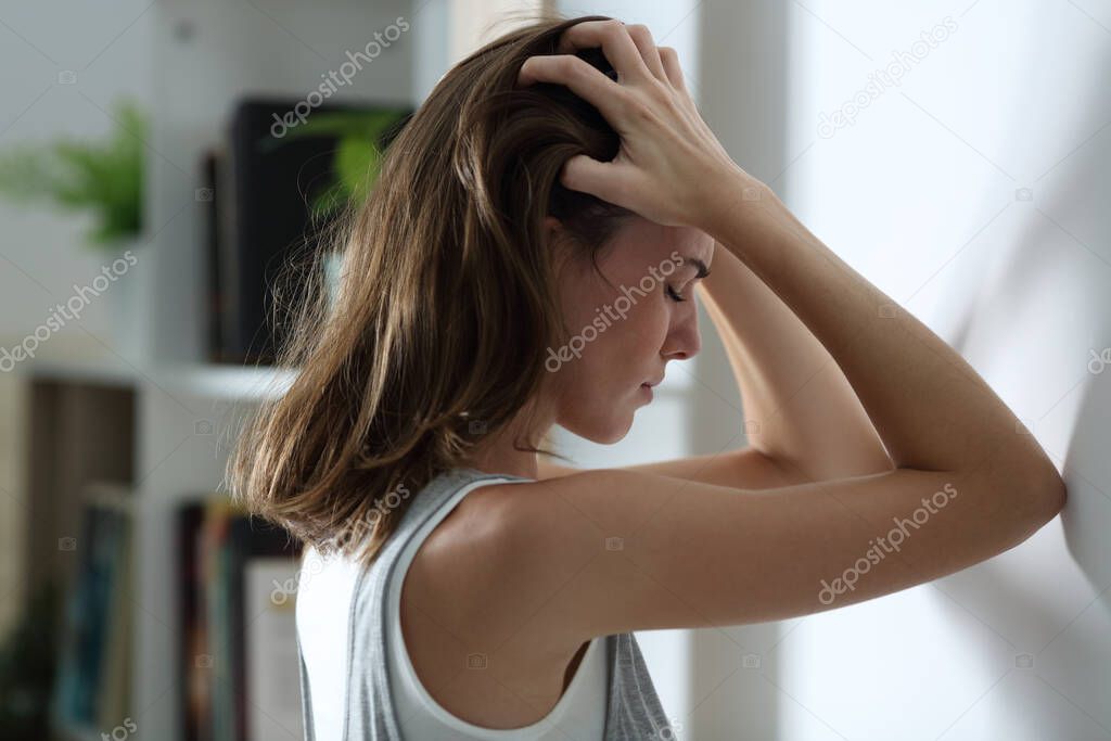 Side view portrait of a sad woman complaining leaning on a wall at home in the night