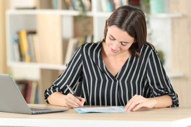 Gülümseyen kadın evdeki masada oturan belgeleri imzalıyor.