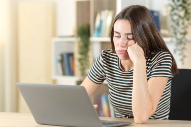 Evde masa başında oturmuş dizüstü bilgisayarla vakit harcayan sıkıcı bir genç.