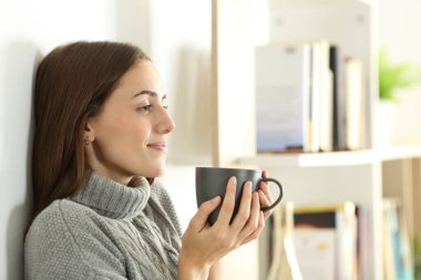 Rahatlamış bir kadının profili kışın elinde kahve fincanı tutarken yüzünü çevirir.