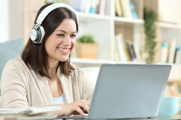 Kulaklıklı Mutlu Bir Kadın Evdeki Bir Masada Dizüstü Bilgisayar Kullanıyor — Stok fotoğraf
