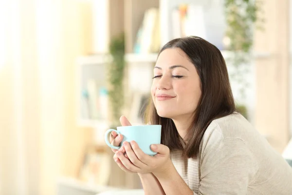 一个心满意足的女人坐在客厅的沙发上 舒舒服服地拿着咖啡杯 — 图库照片