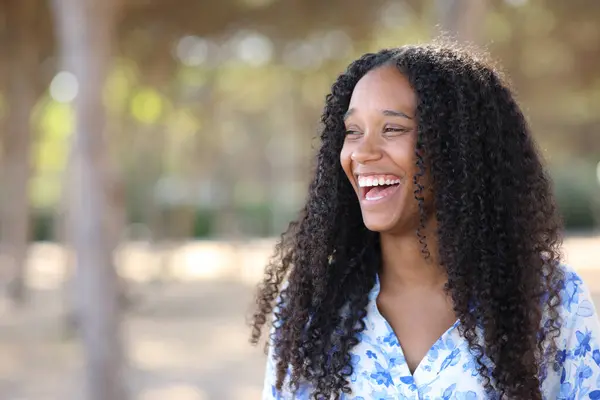 Joyful black woman laughing loud standing in a park looking at side