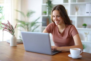 Evde bir odada dizüstü bilgisayar kullanan mutlu bir kadın.