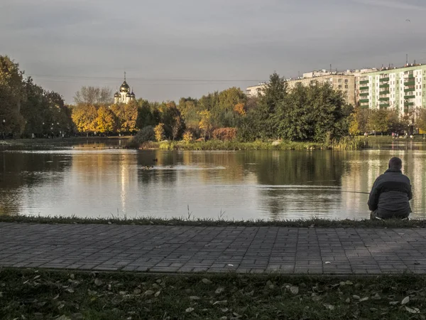 Hombre pescando. Tiempo de otoño, otoño en la ciudad, paisaje urbano de otoño con un estanque, gente caminando y otra diversión —  Fotos de Stock