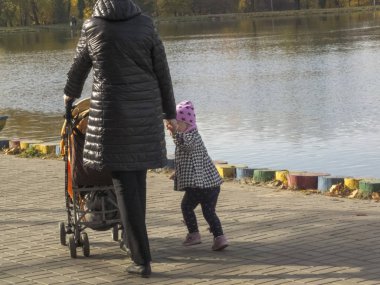 Çocuklu bir kadın. Küçük kız sonbahar parkında yürüyor. Sonbahar saati, şehirde sonbahar, bir gölet ile kentsel sonbahar manzara, insanlar yürüyüş ve diğer eğlenceli