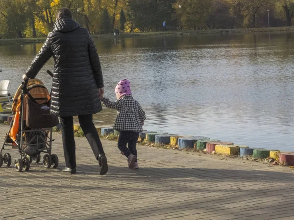 Nő egy gyerekkel. Kislány sétál az őszi parkban. Őszi idő, ősszel a városban, a városi őszi táj egy tó, az emberek gyalog és más szórakoztató — Stock Fotó